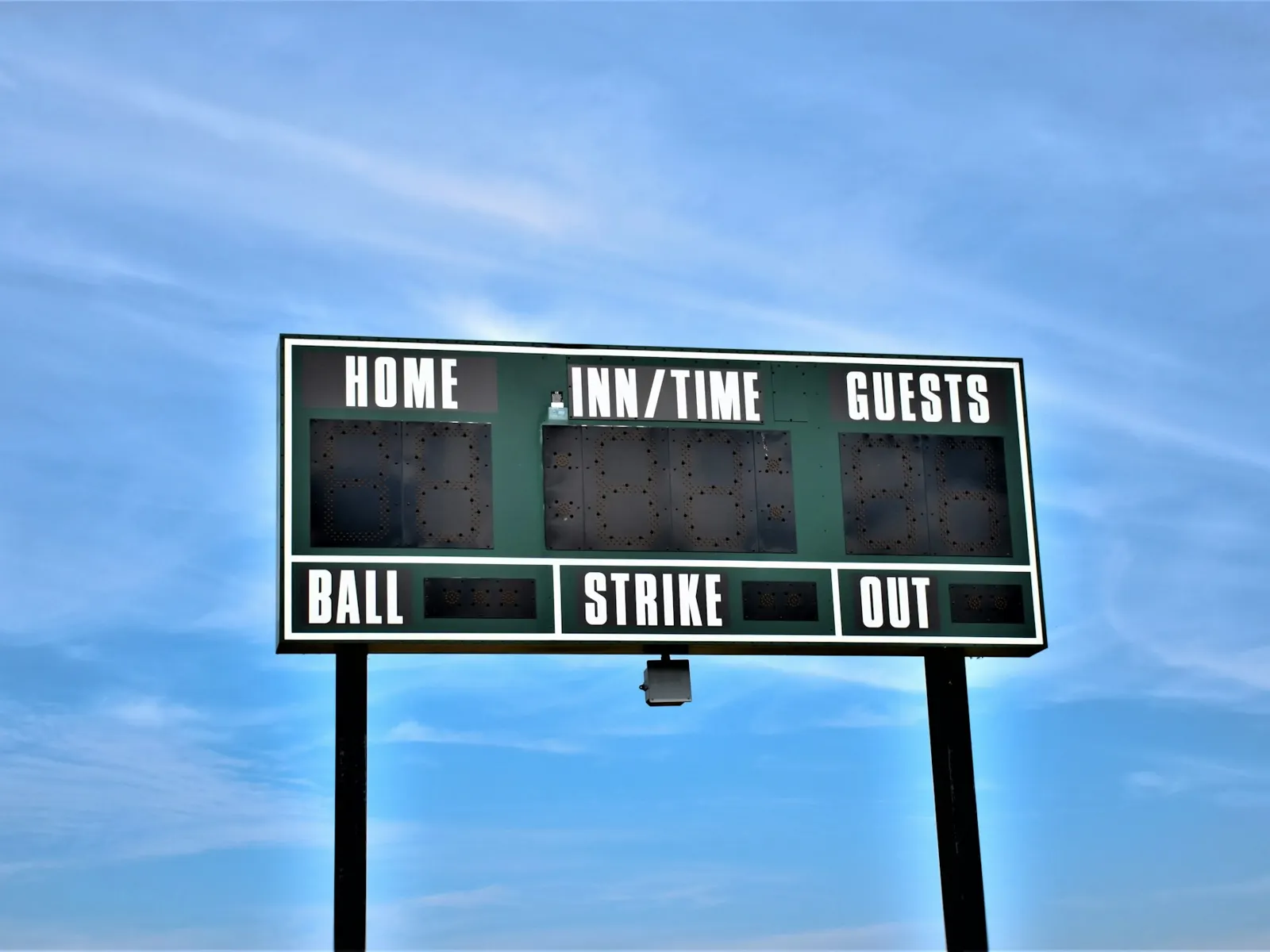 Outdoor sports scoreboard display with home and guest panels on posts under blue sky