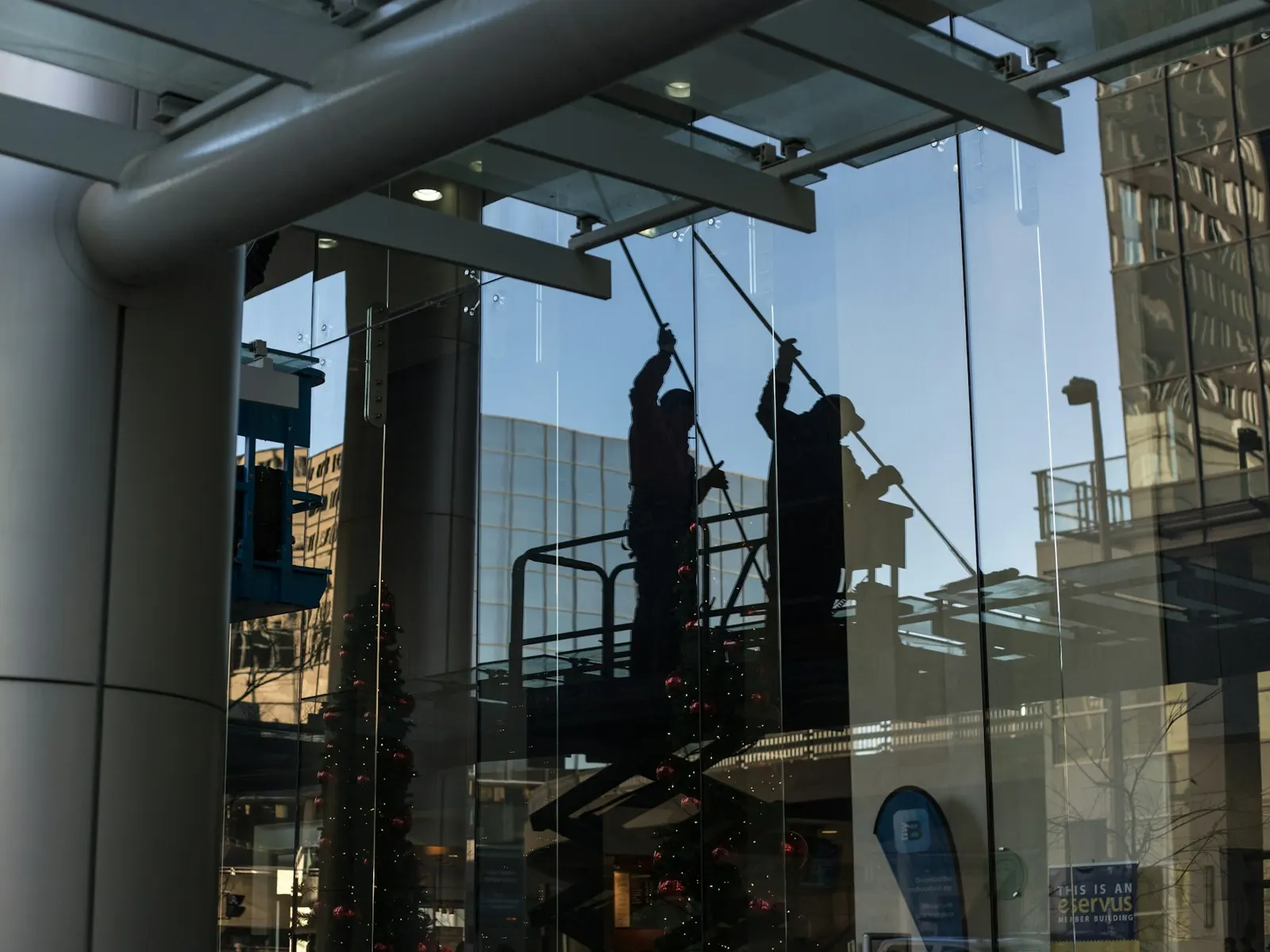 Workers on a platform cleaning a large glass shopfront facade with long poles