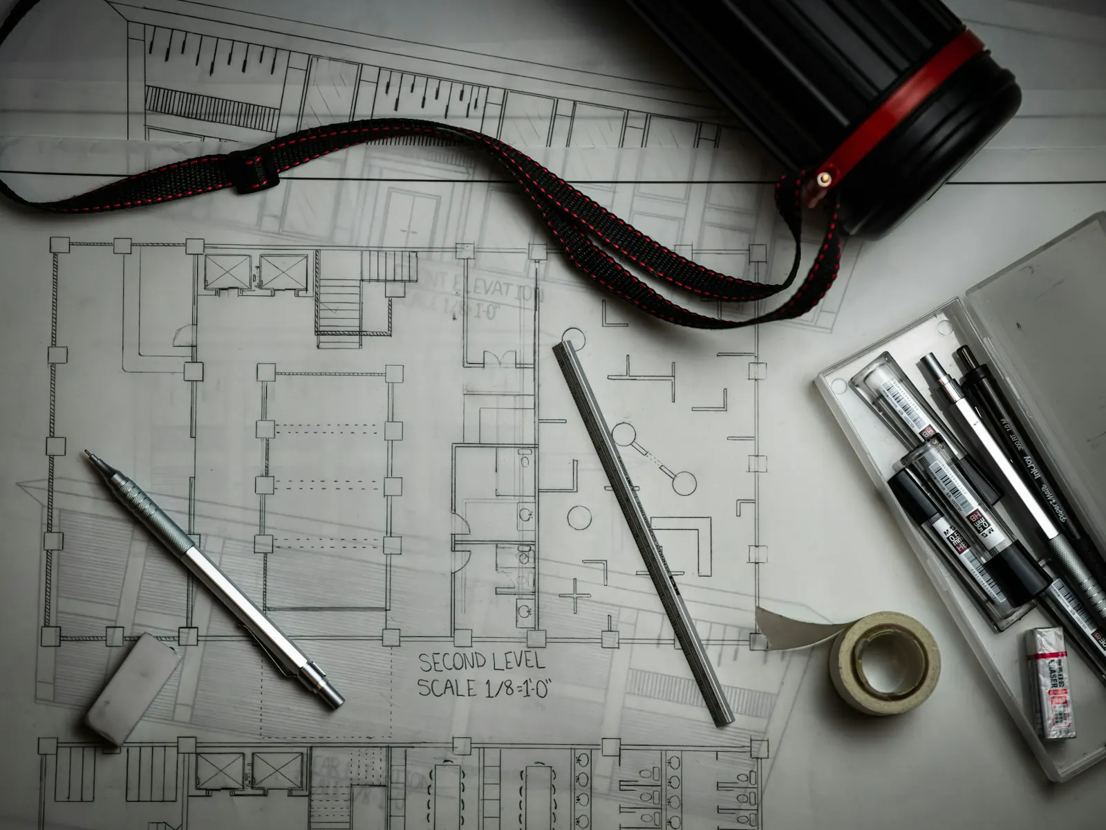 Technical shop drawings and floor plans laid out with pens, pencils and a drawing tube