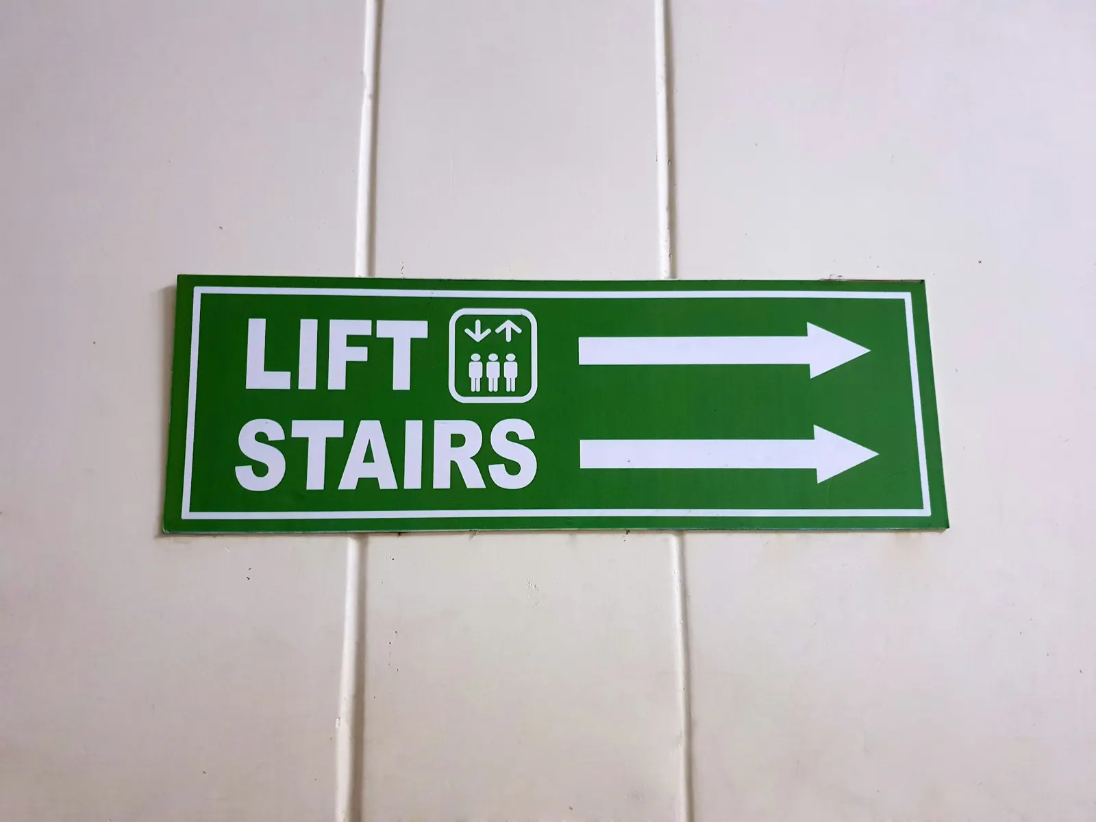 Green lift and stairs directional sign with arrows fixed to a white wall