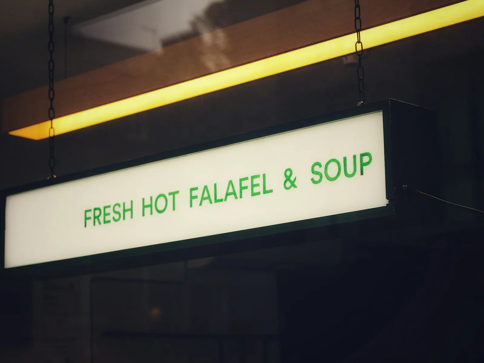 Hanging light box sign suspended from the ceiling of a dimly lit food outlet