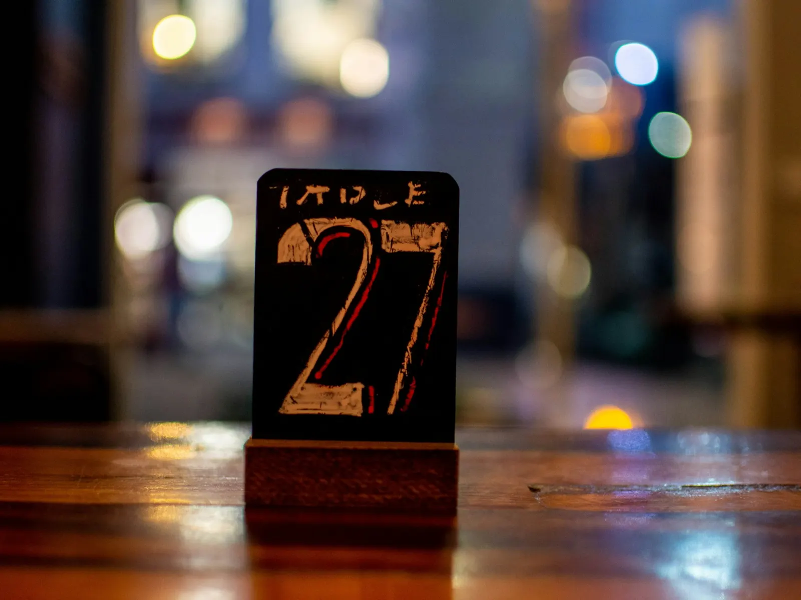 Table number sign showing 27 standing on a polished wooden restaurant table at night