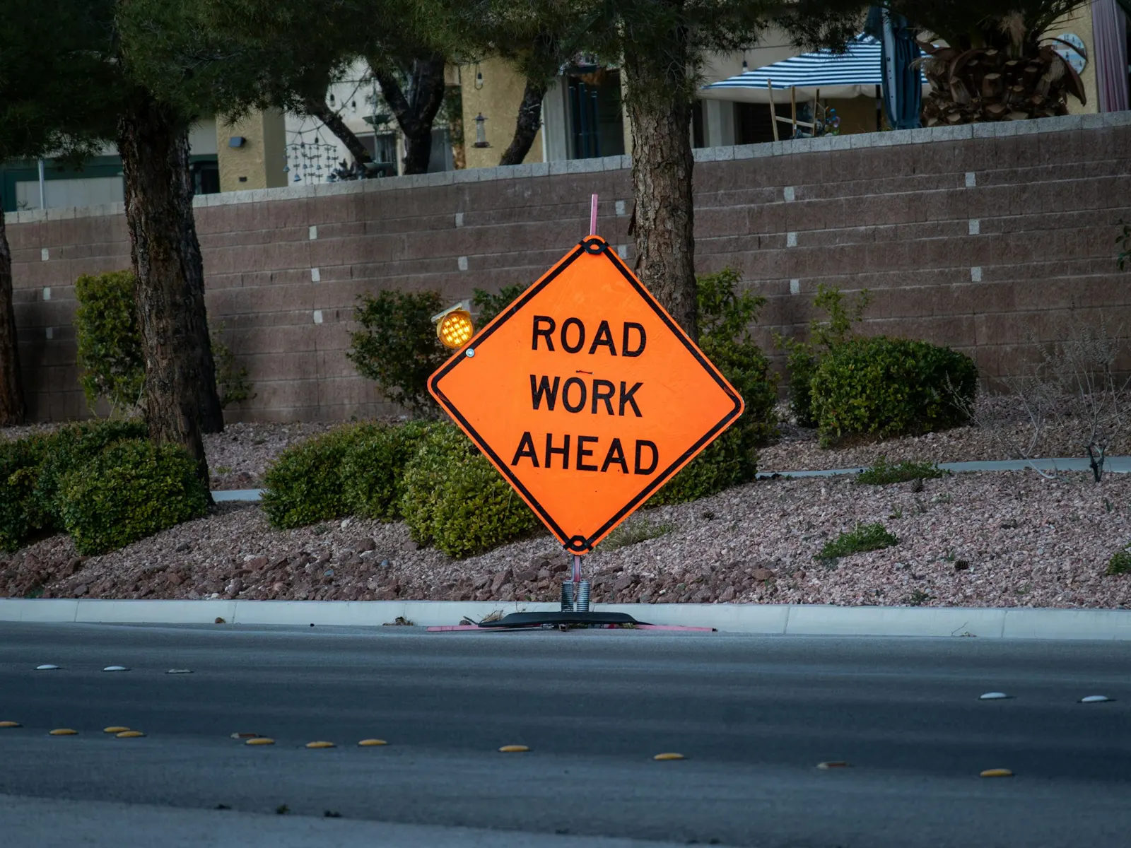 Orange temporary road work ahead sign on a stand beside a roadside kerb