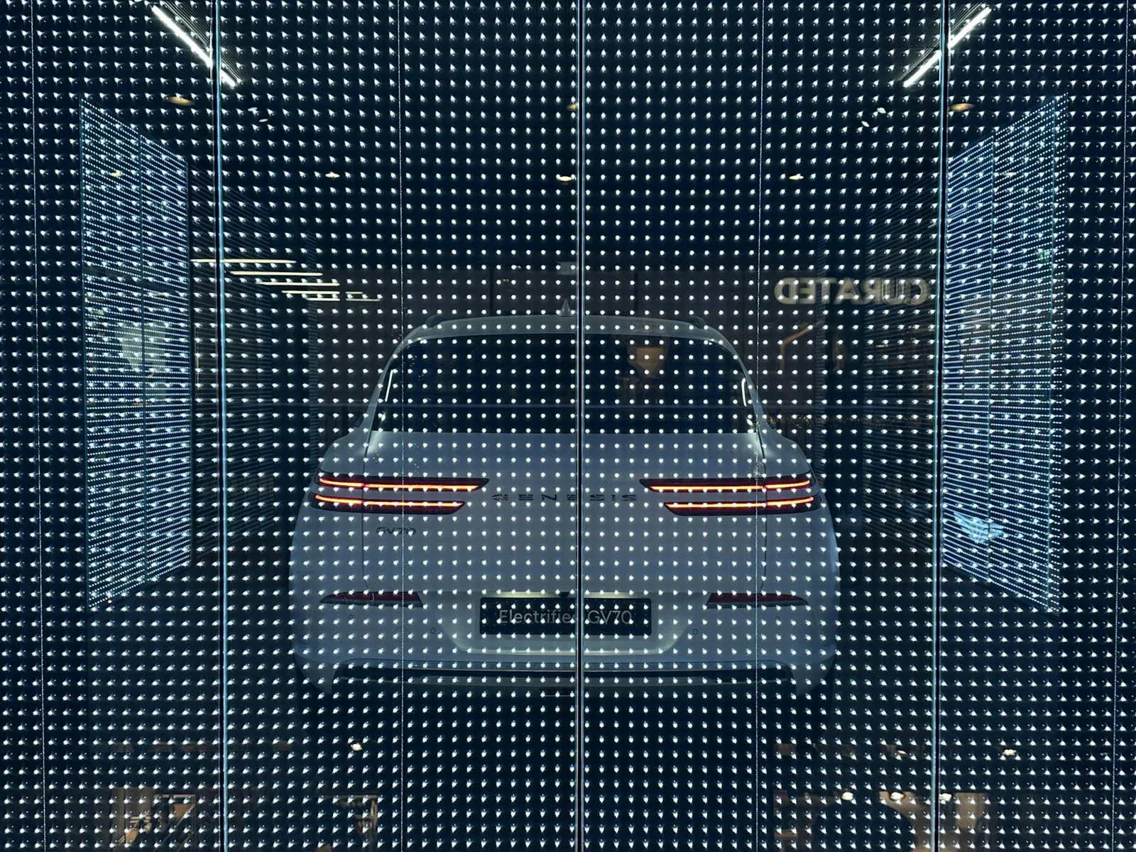Transparent LED mesh screen with a car showroom visible through the glowing pixels