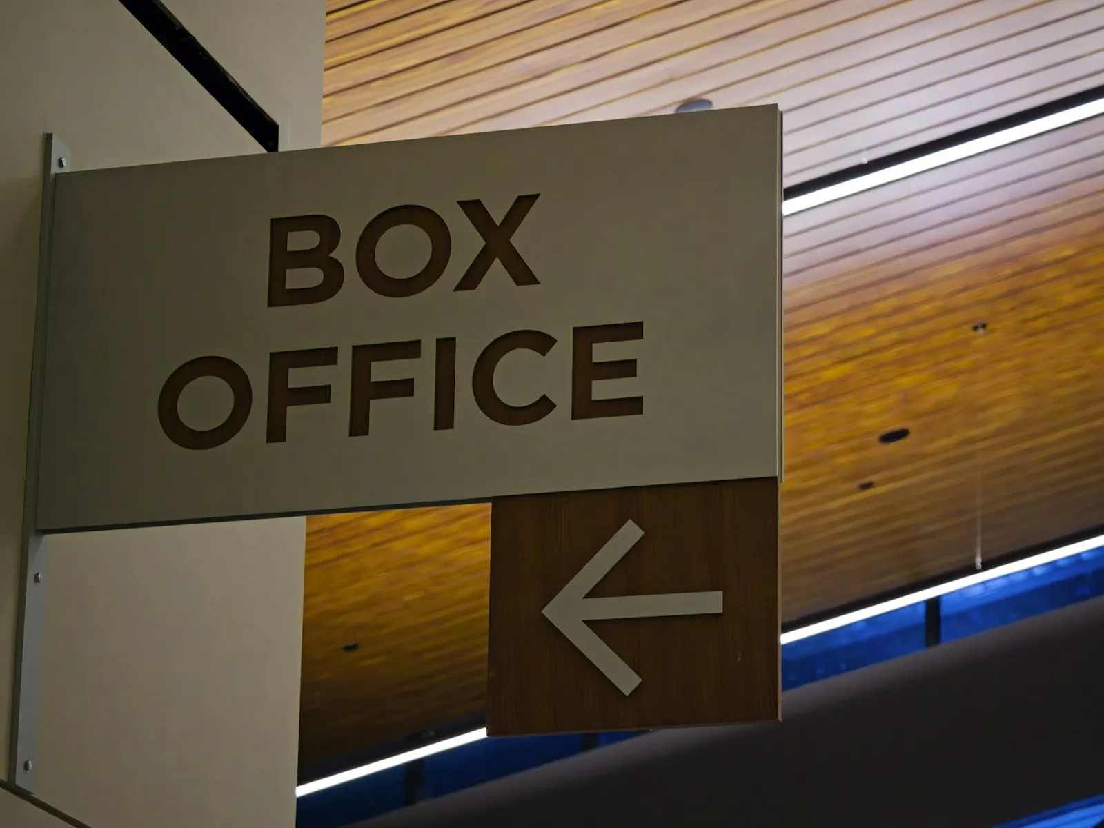 Wall-mounted directional sign with bold lettering and a left arrow beneath a wooden ceiling