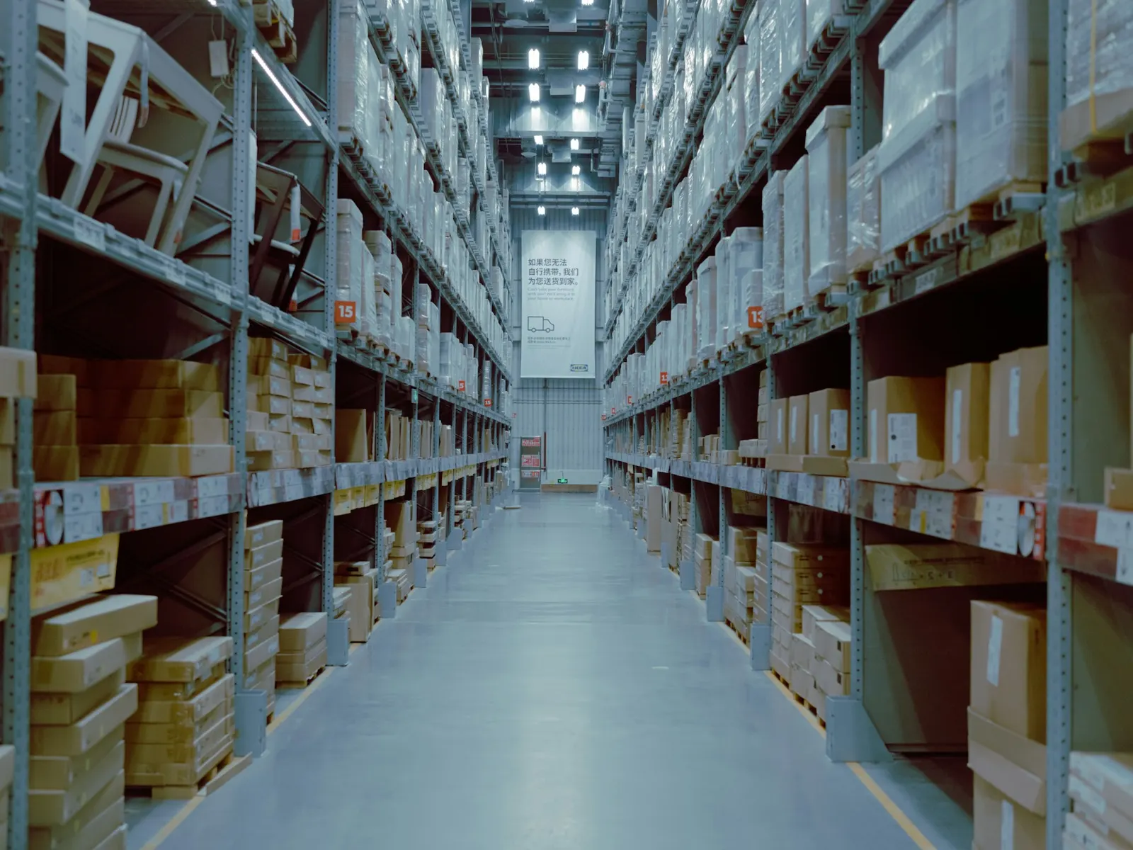 Long warehouse aisle between tall pallet racks with labelled shelf locations and boxes