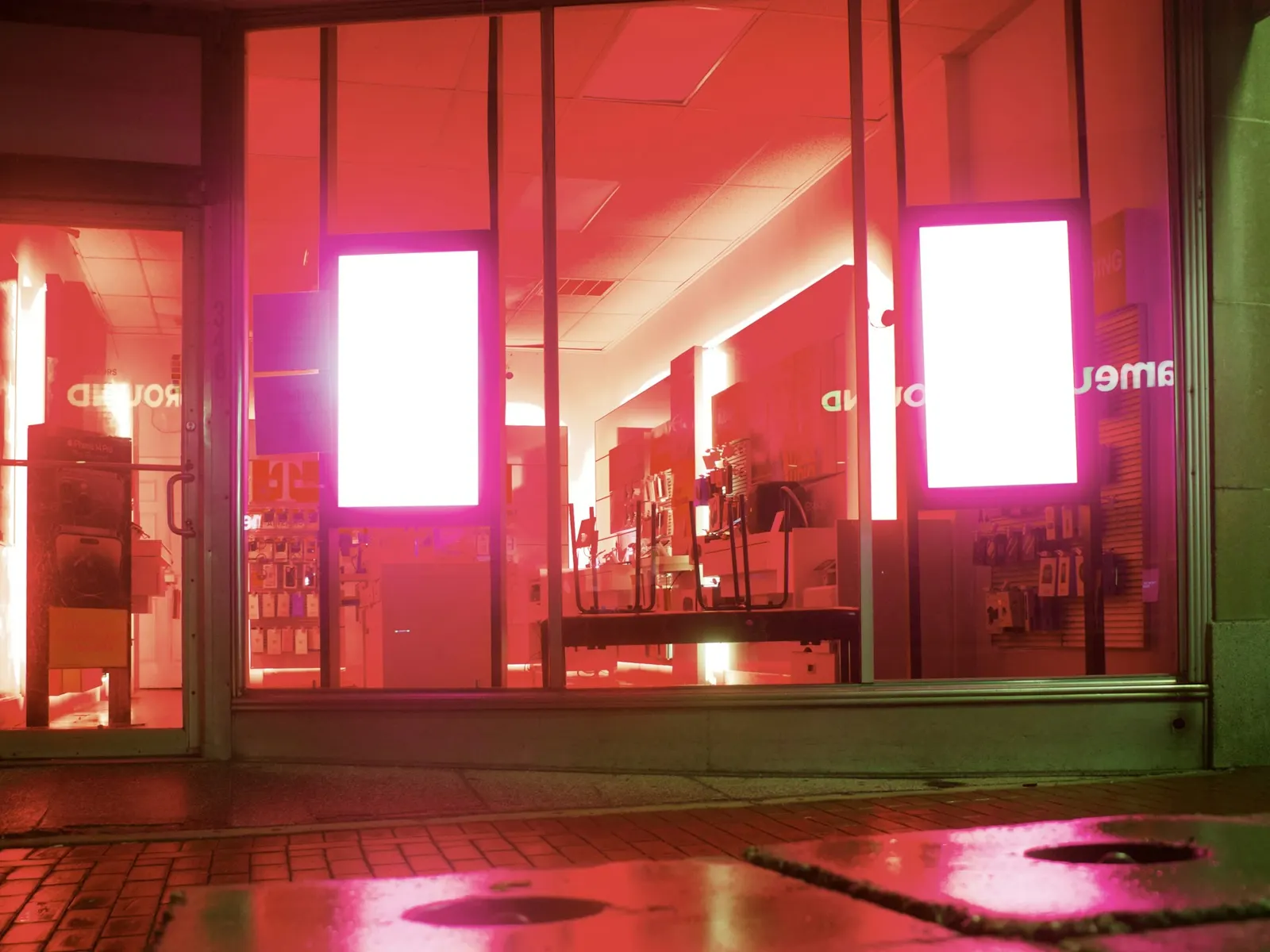 Two bright portrait display screens glowing inside a shopfront window at night