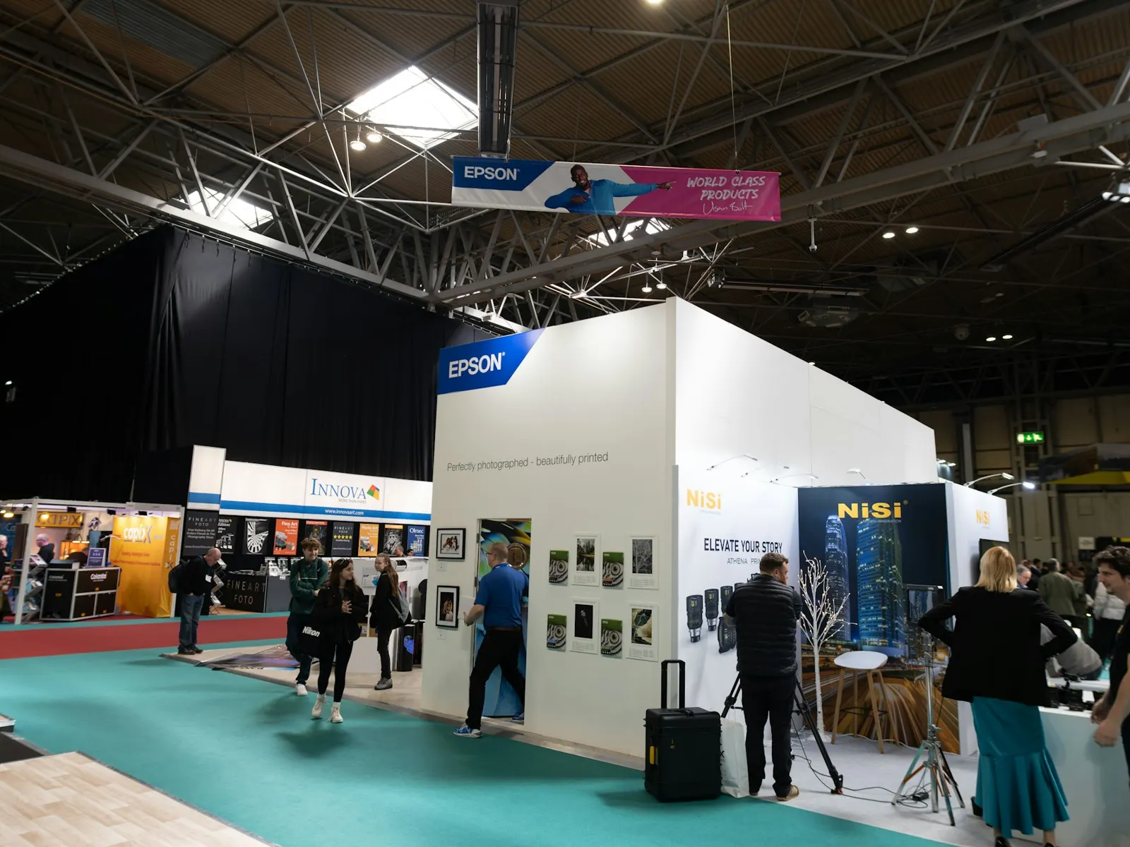 Exhibition hall with printed display stands and promotional graphics along a busy aisle
