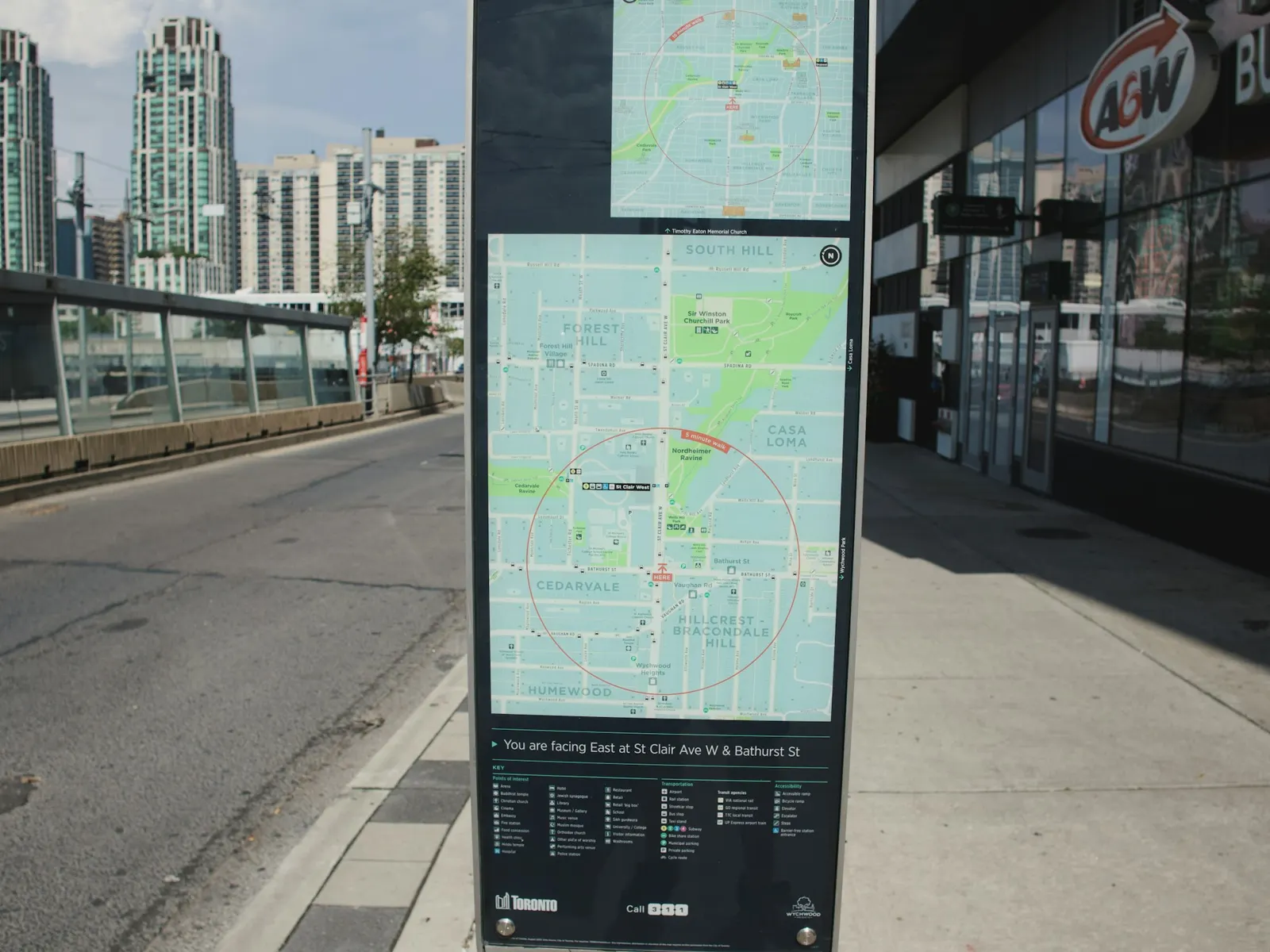 Tall street map sign with a city plan panel standing on an urban sidewalk