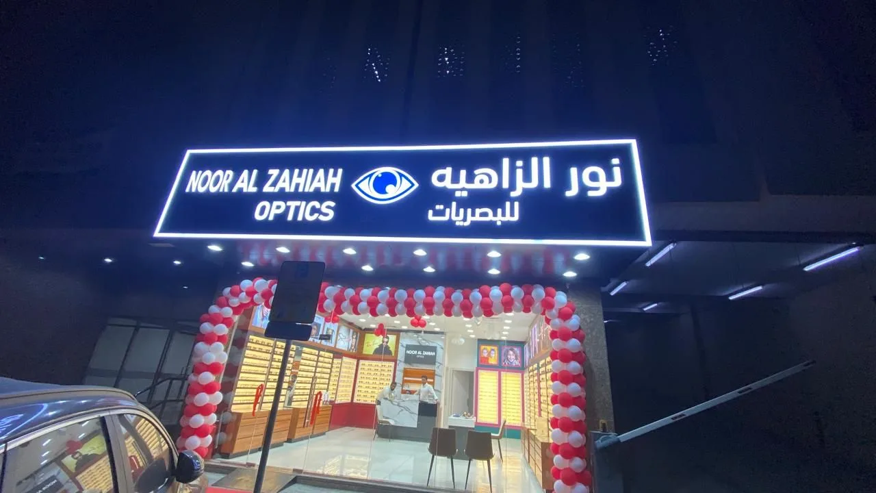 Lit bilingual front-lit letter sign on an optics shop at night with opening balloons